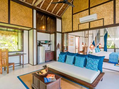 Camera d'hotel tropicale aperta con arredamento rustico in legno e divano con cuscini blu.