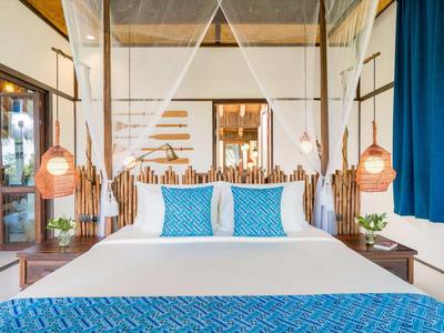 Camera d'hotel moderna con letto matrimoniale, biancheria blu e bianca e lampade sospese.