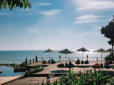 Entspannter Poolbereich mit Liegestühlen und Schirmen, Blick aufs Meer bei klarem Himmel.