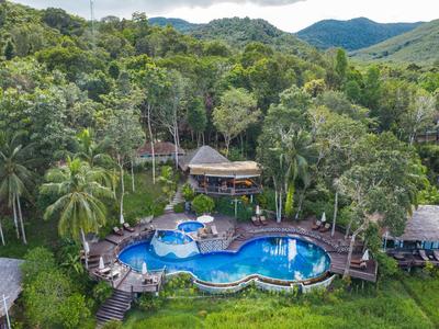 Hotelanlage mit geschwungenem Pool inmitten dichter tropischer Vegetation und Hügeln im Hintergrund.