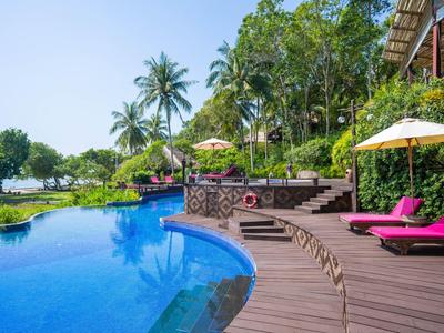 Hotelpool mit Liegestühlen, Sonnenschirmen und tropischer Bepflanzung am Meer.