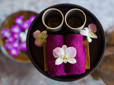 Zwei lila Handtücher mit weißen Orchideen und zwei Tassen auf einem schwarzen Tisch, umgeben von Blumen.