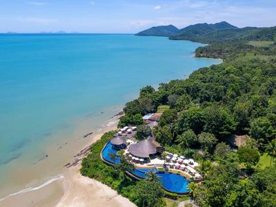 Hotelanlage mit Pool am Strand, umgeben von dichtem Grün und Bergkulisse im Hintergrund.