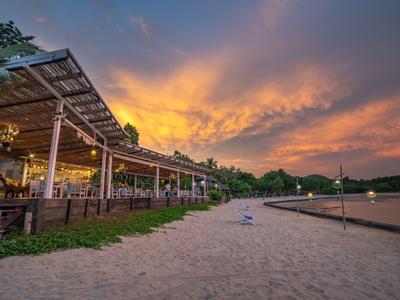 Strand mit Sand, einer überdachten Terrasse und einem farbenfrohen Sonnenuntergang am Hotel.