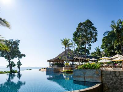 Infinity-Pool mit Blick auf das Meer neben einem Hotel mit Sonnenschirmen und Palmen.