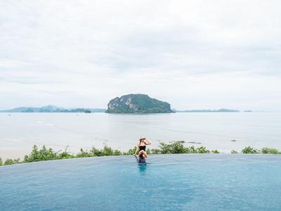 Unendlicher Pool mit Blick auf das Meer und eine Insel im Hintergrund bei bewölktem Himmel.