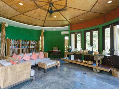 Area lounge accogliente con pareti verdi, mobili in vimini e libreria in un hotel.