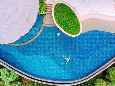 Vista di una piscina con acqua blu, un'isola coperta di piante e una struttura di ombrellone bianco.
