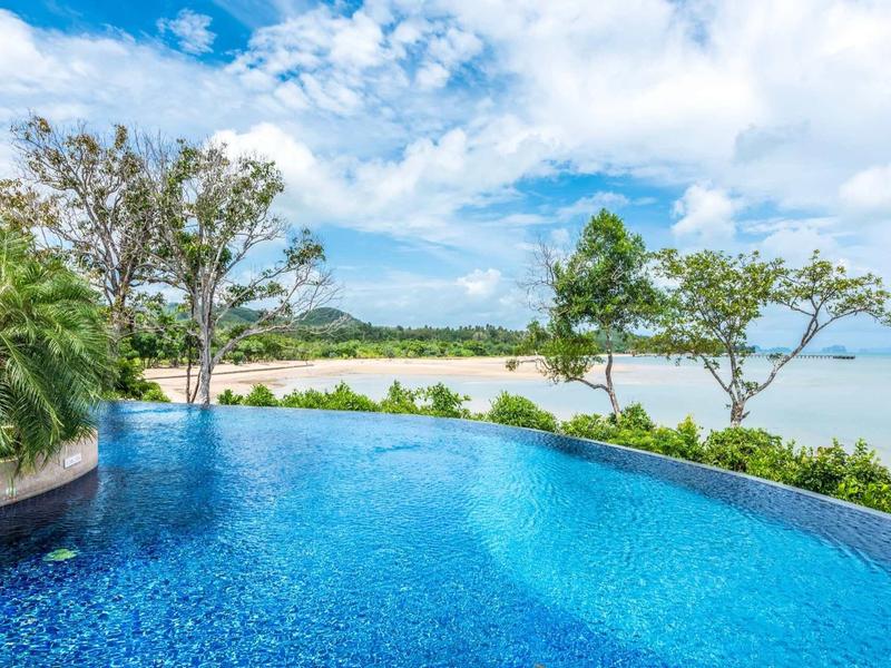Piscina a sfioro con vista sulla spiaggia e sull'oceano sotto un cielo azzurro.