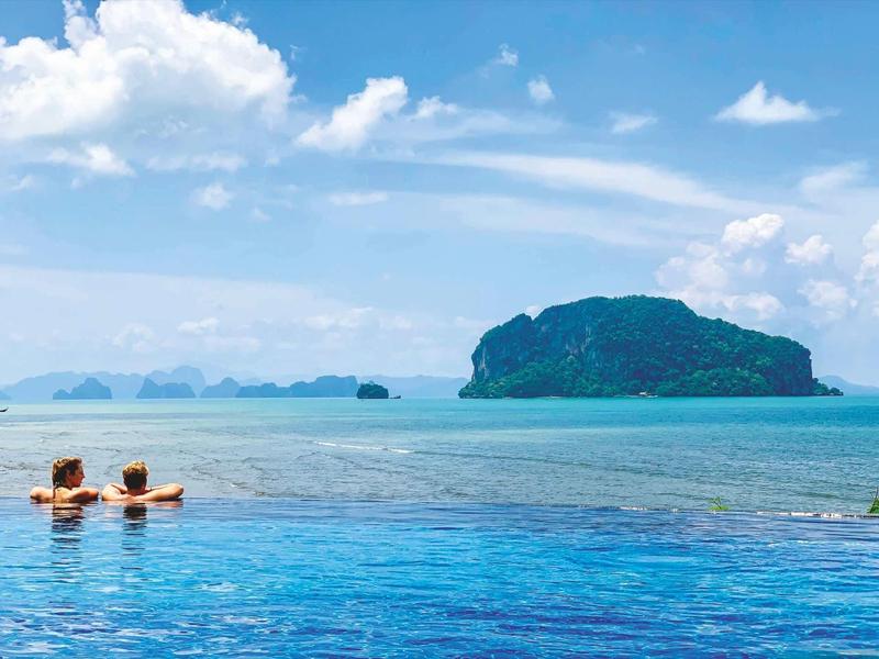 Due persone si rilassano in una piscina a sfioro con vista sul mare blu e un'isola.