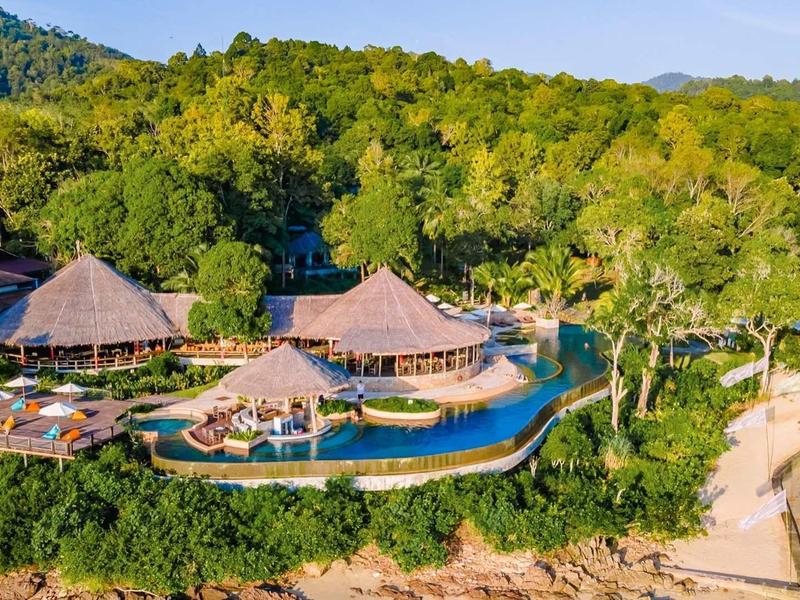 Resort di lusso con piscina, lettini e spiaggia vicino a collina boscosa.