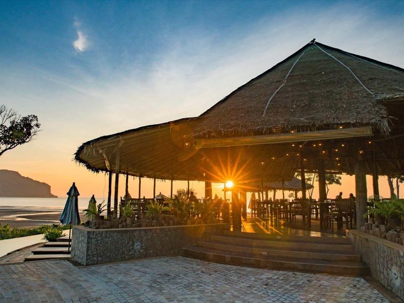 Tramonto su un bar sulla spiaggia aperto con tetto di paglia vicino al mare.