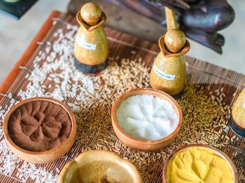 Vassoio di legno con cinque ciotole contenenti diverse spezie e un fiore viola.