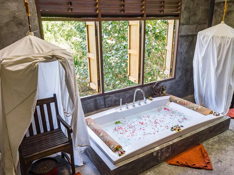 Un bagno di lusso con una vasca da bagno piena, sedia di legno e tende alle finestre.