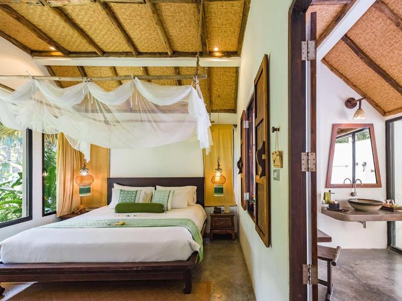 Camera luminosa con zanzariera e mobili in legno in un hotel tropicale.