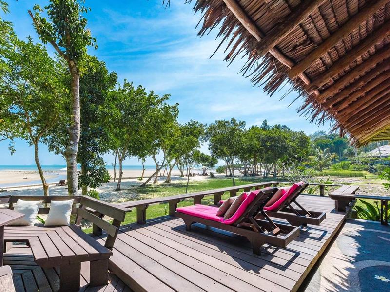 Deck in legno con lettini e tavoli con vista sulla spiaggia e sul mare sotto un cielo blu.