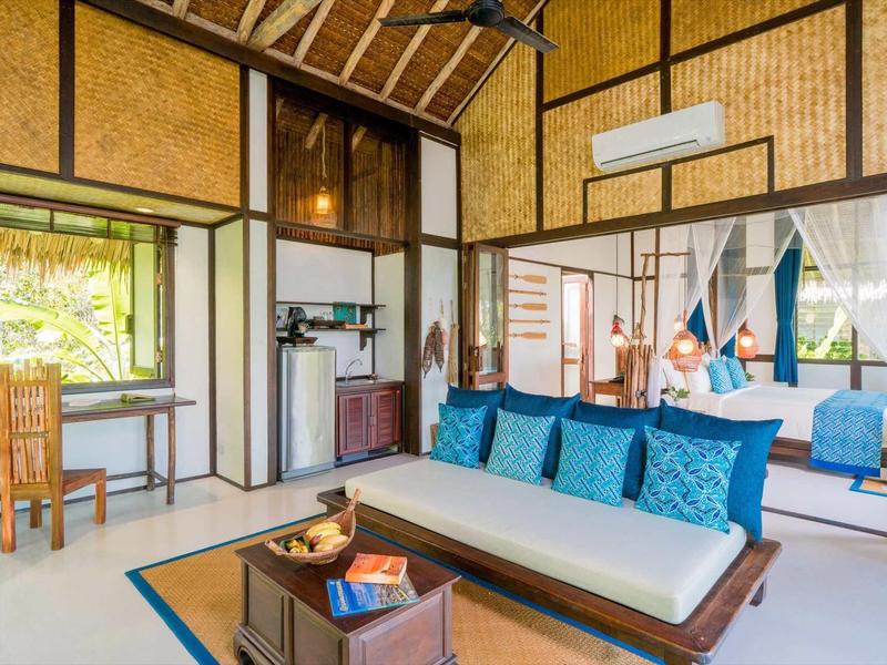 Camera d'hotel tropicale aperta con arredamento rustico in legno e divano con cuscini blu.