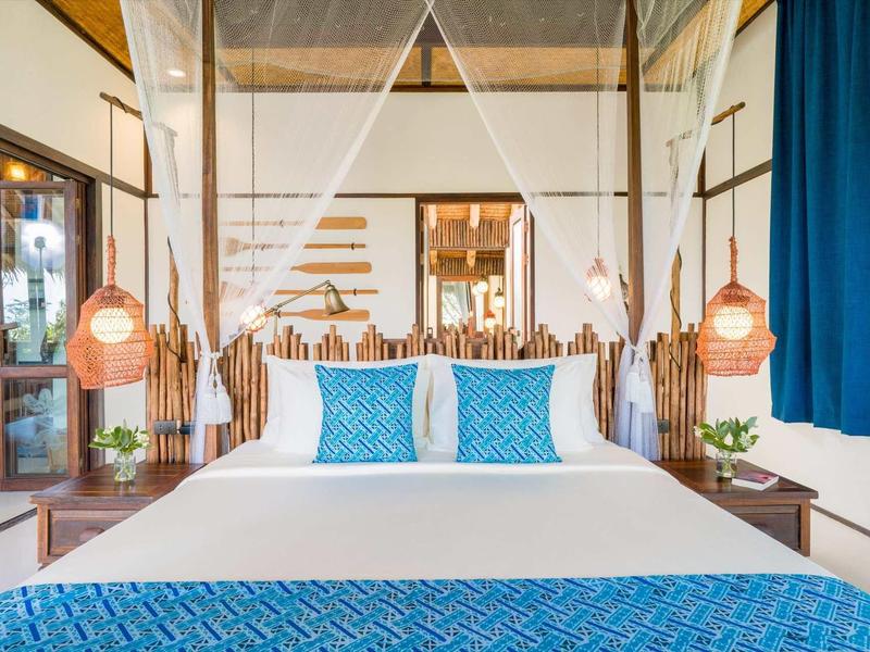 Camera d'hotel moderna con letto matrimoniale, biancheria blu e bianca e lampade sospese.