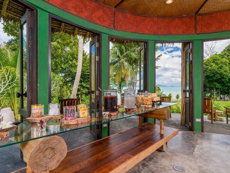 Area colazione aperta con mensole di vetro, panca in legno e vista sul giardino tropicale.