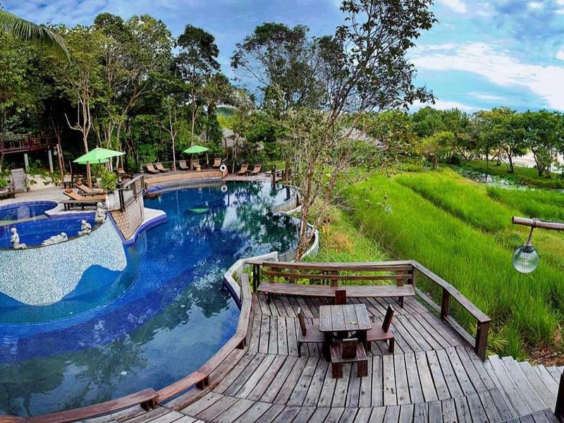 Piscina esterna moderna con decking in legno e area salotto, circondata da un paesaggio verdeggiante.