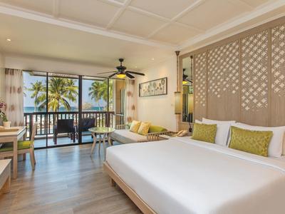 Bright hotel room with king bed, balcony, and views of palm trees and ocean.