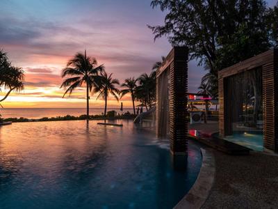 Infinity pool with palm trees and benches at sunset at the beach hotel.
