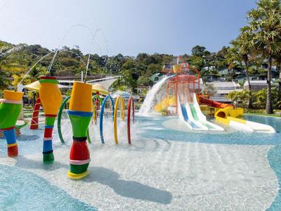 Colorful water play structures and slides in a sunny pool area with palm trees.