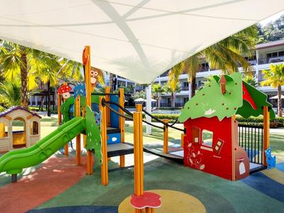 Colorful playground with slide and climbing frame under sunshade in a tropical hotel garden.