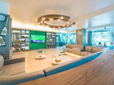 Moderní hotelový salonek s velkými okny, pohodlnými sezením a televizí na stěně.