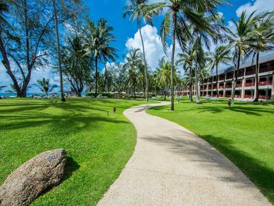 Curved path through green grass with palm trees and hotel building in the background.