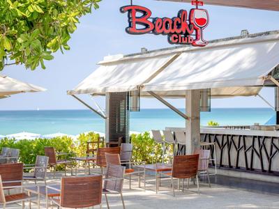 Beach bar with chairs and tables, ocean view and green foliage in the background.