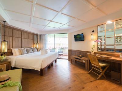 Světý hotelový pokoj s velkou postelí, dřevěným nábytkem a balkonem s výhledem ven.