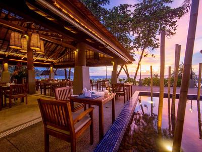 Otevřená restaurace s dřevěným nábytkem a výhledem na bazén při západu slunce.