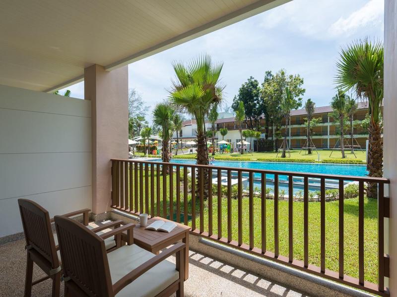 Balcony with two chairs overlooking a pool and palm trees in a hotel setting.