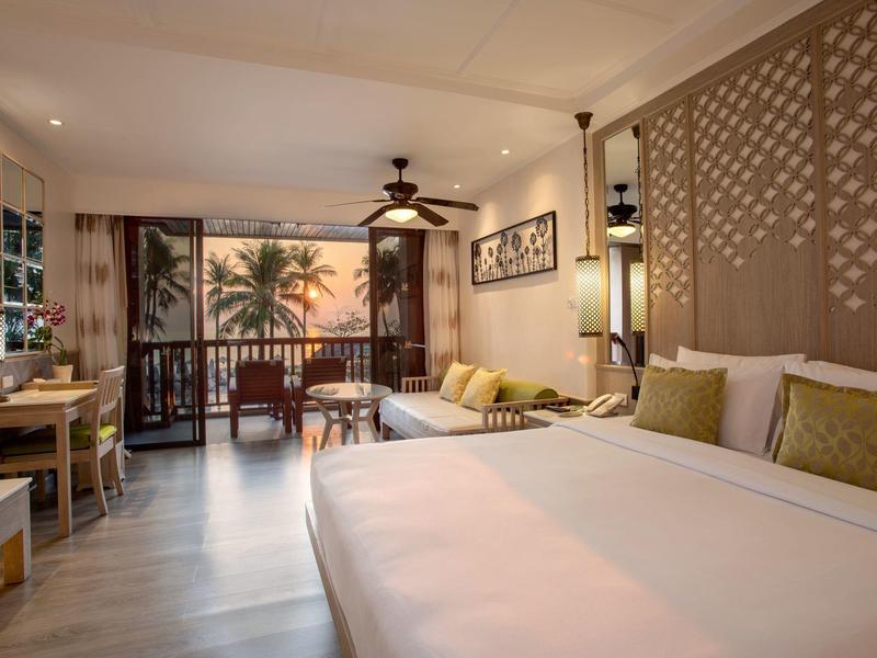 Cozy hotel room with large bed, balcony, and sea view at sunset.