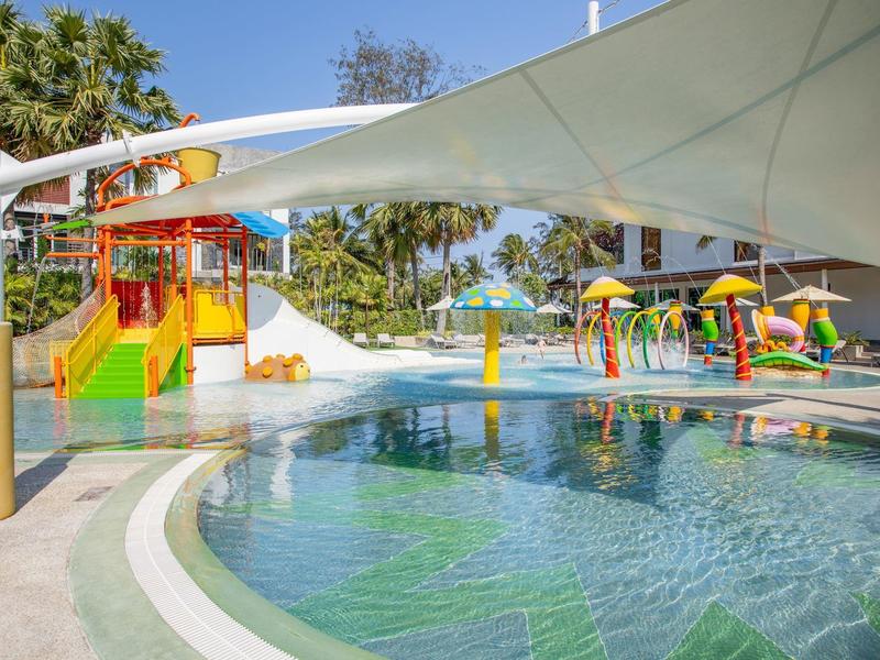 Colorful water playground with slides and sprays beside a pool under a sunshade.