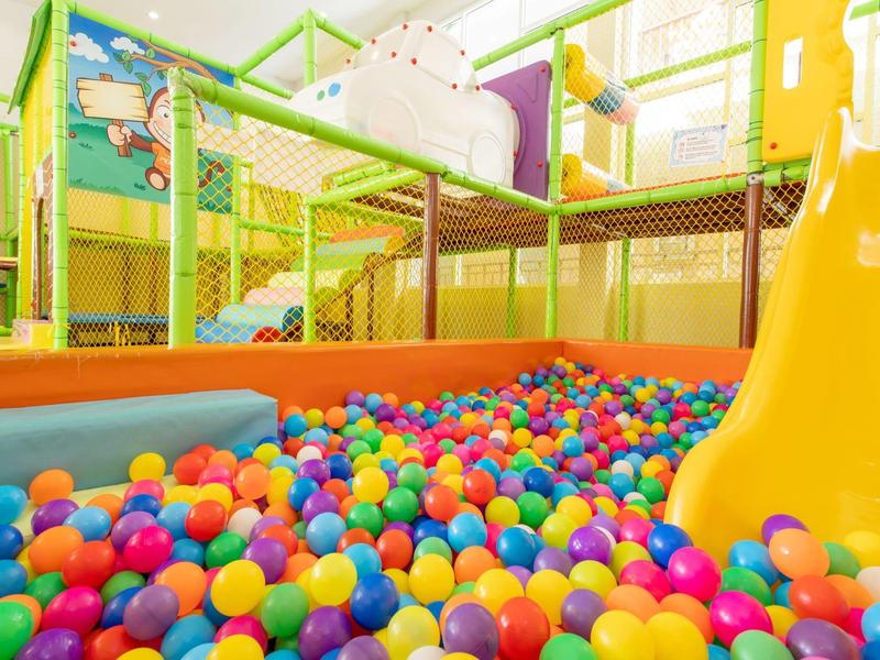 Colorful ball pit with yellow slide in bright indoor play area.