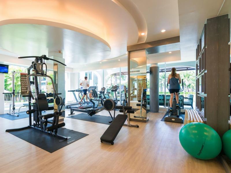 Bright modern gym with equipment, large windows, and wooden flooring in a hotel.