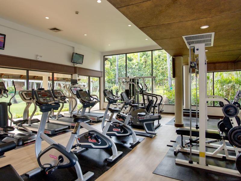 Modern fitness equipment in a bright hotel gym with large windows.