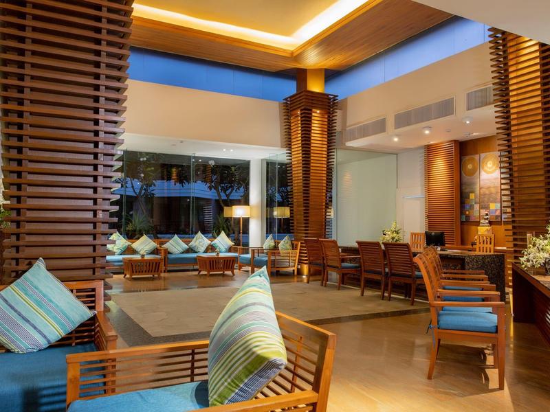 Elegant hotel lobby with wooden furniture, cushions, and warm lighting accents.