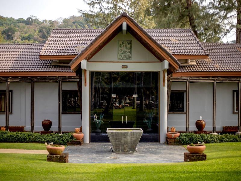 Modern building with glass facade and brown pitched roof, surrounded by green lawn.