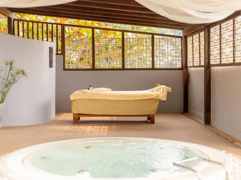 Bright spa lounge with warm lighting, freestanding bathtub, and hot tub in an enclosed space.