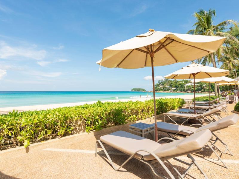 Beach loungers with umbrellas on a tropical sandy beach under a blue sky.