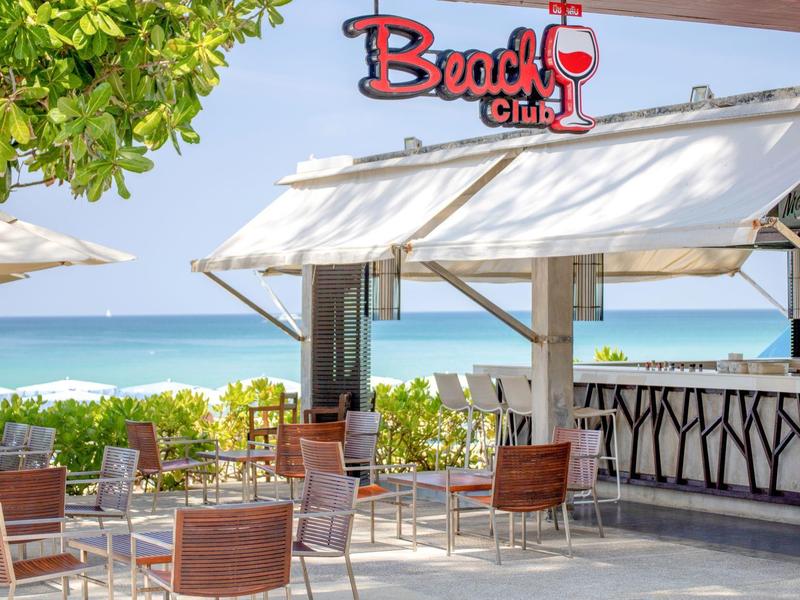 Beach bar with chairs and tables, ocean view and green foliage in the background.