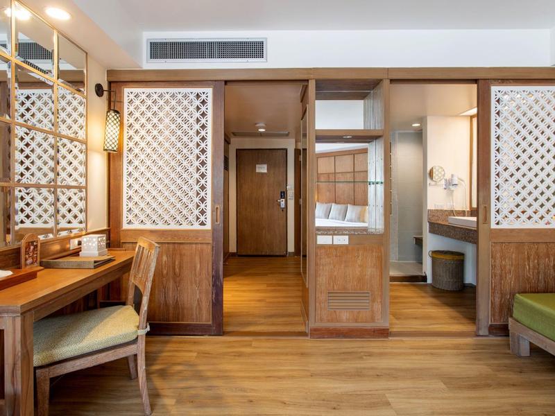 Hotel room with wooden furniture, desk, chair, and open bathroom with wooden paneling.