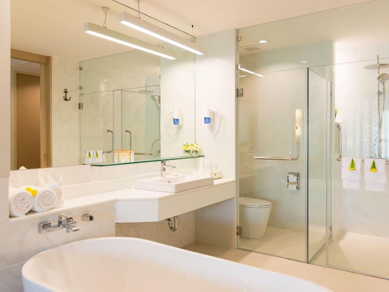 Bright hotel bathroom with bathtub, glass shower, sink, and large mirrors.