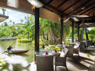 Terrasse couverte avec des tables au bord de la rivière, entourée d'une végétation luxuriante et d'un bateau sur l'eau.