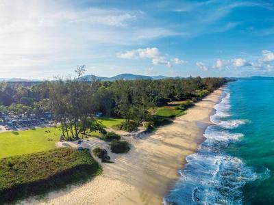 Dlouhá písečná pláž s tyrkysovou vodou a zelenou vegetací podél pobřeží.