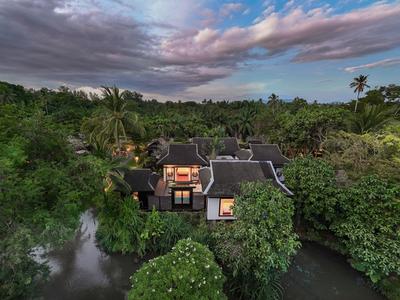 Luksusowa willa otoczona gęstą tropikalną roślinnością i wodnymi drogami o zachodzie słońca.