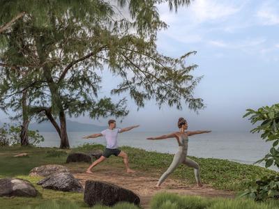 Dwie osoby ćwiczą jogę na zewnątrz z widokiem na morze pod pochmurnym niebem.
